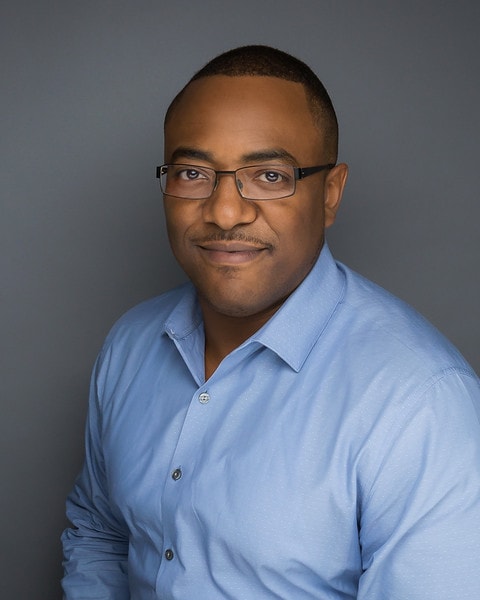 This is a headshot of Jason wearing a blue button down shirt against a grey background.