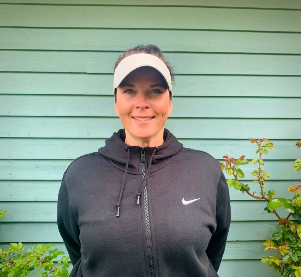 This is an image of Crystelle Fisher wearing a black hoodie against a seafoam green house.