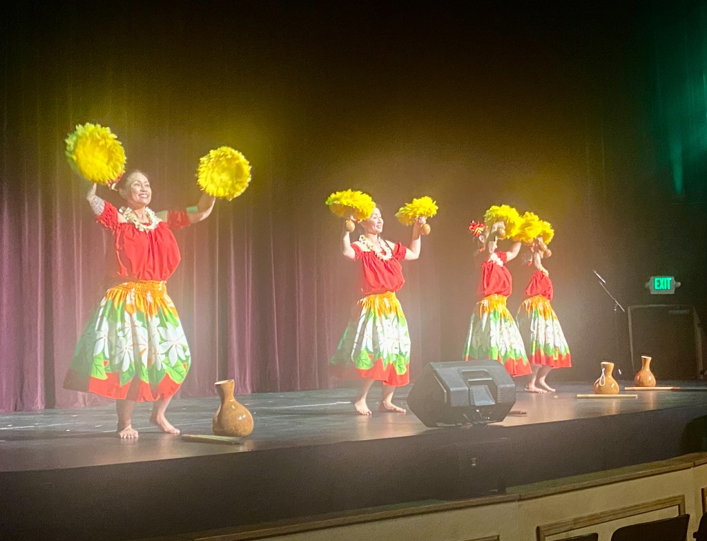 Four dancers dressed in red shirts, and colorful skirts doing a traditional dance.