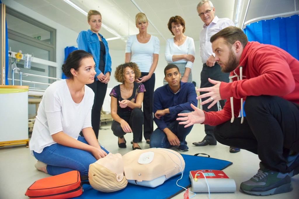 The first picture is a a mixed age group listen to their tutor as he shows the procedure involved to resuscitate using a defibrillator .
The second picture is of two people practicing CPR