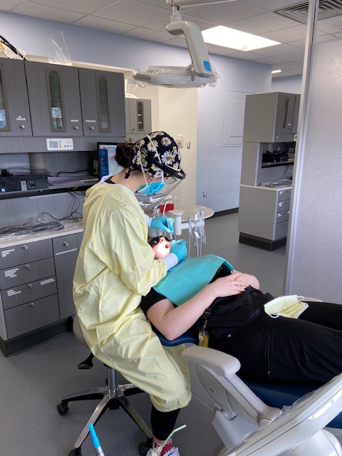 A person in yellow scrubs is practicing dental hygiene on a patient