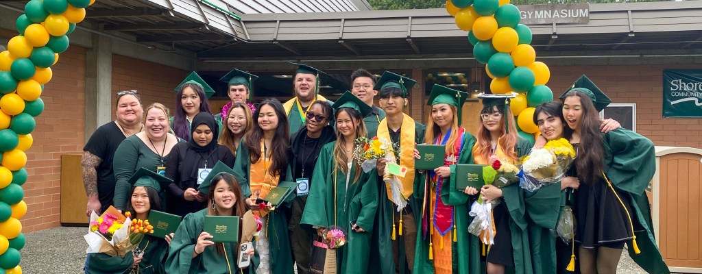 Smiling graduates under an arch made of green and yellow balloons.
