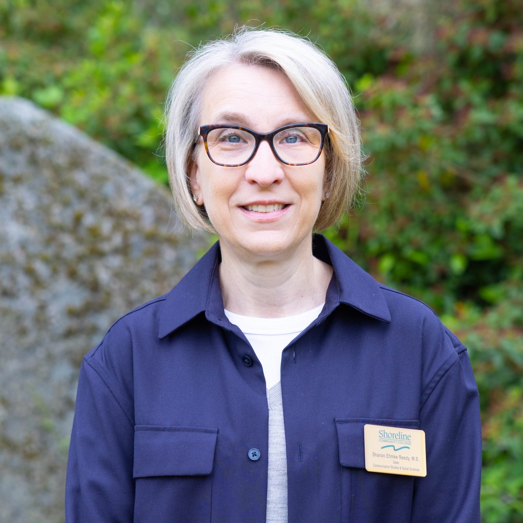 Headshot of Shanon wearing a white tshirt and a navy button-down over it
